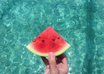hand_holding_watermelon_with_blue_swimming_pool_water_in_the_background hand_holding_watermelon_with_blue_swimming_pool_water_in_the_background