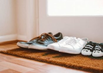 three_pairs_of_shoes_placed_by_a_white_door_on_a_brown_mat three_pairs_of_shoes_placed_by_a_white_door_on_a_brown_mat